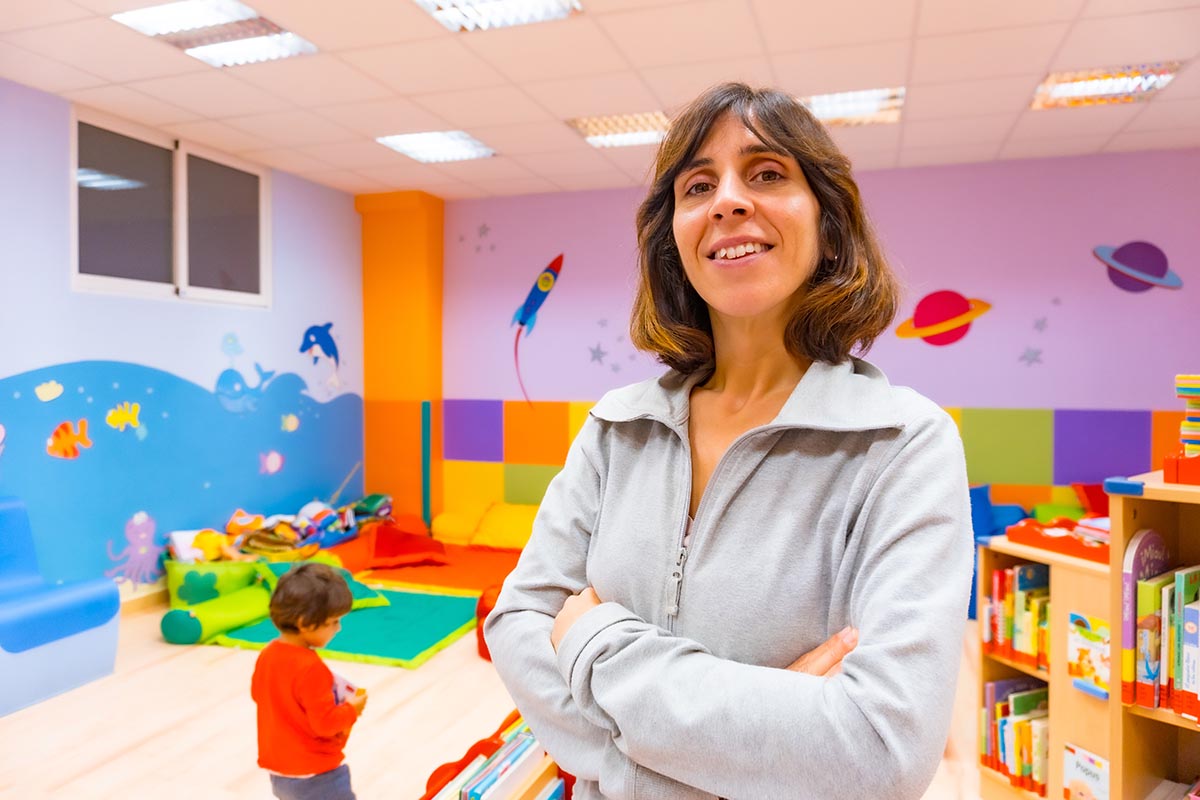 Portrait of a kindergarten or early childhood education teacher inside a kindergarten, with a child playing in the background